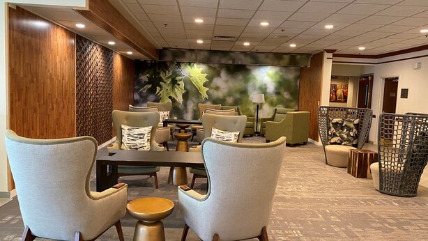 A hotel lobby with a central dining area featuring a round table and chairs, surrounded by sofas and a patterned wall mural.