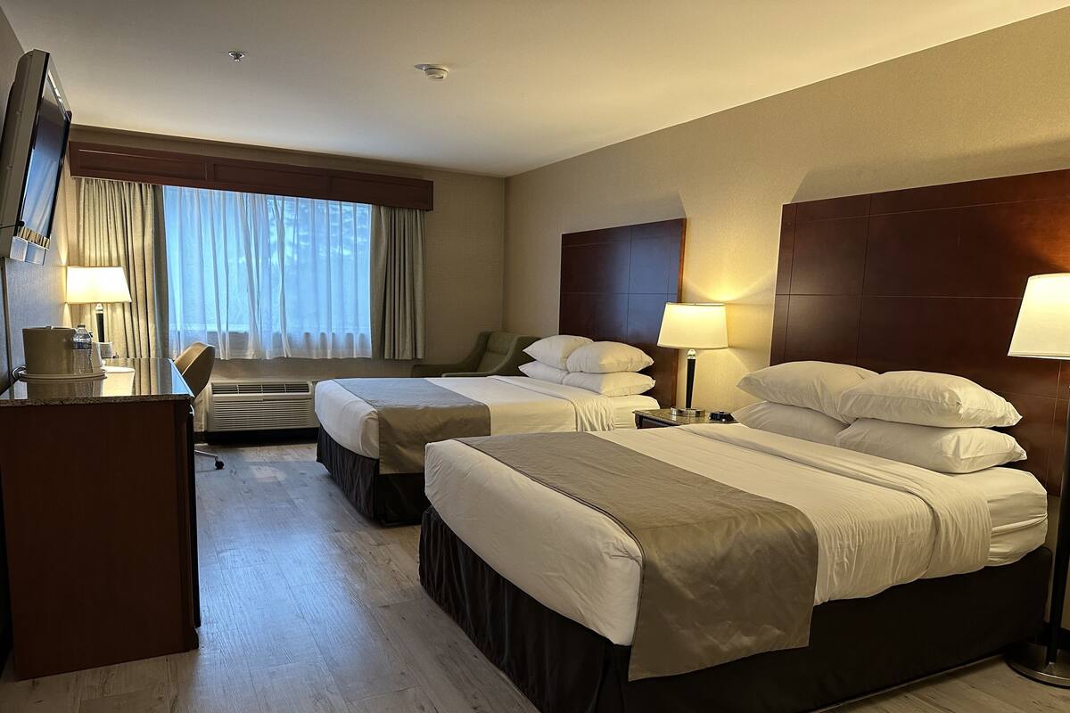 Habitación de hotel con dos camas, un escritorio, una silla, una lámpara y una ventana con cortinas.