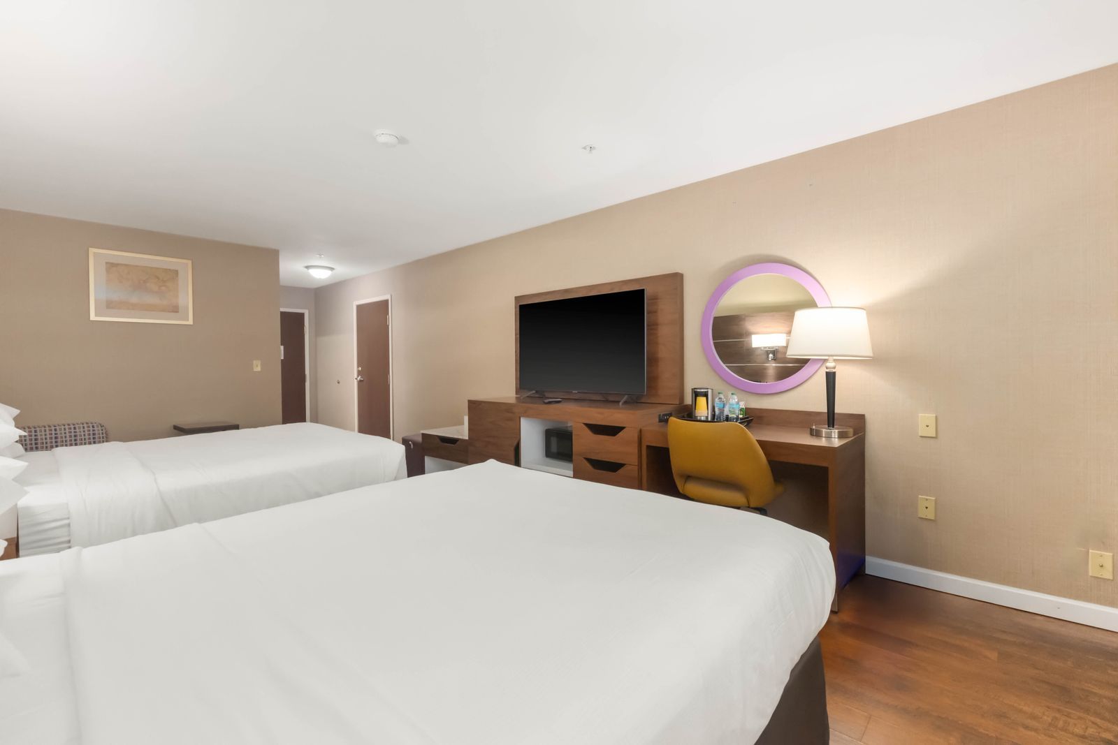 Habitación de hotel con dos camas, un escritorio con computadora, televisor y baño con espejo y lámpara.