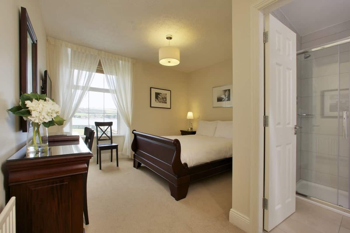 A bedroom with a bed, bedside table, lamp, chair, and a desk with a vase of flowers.