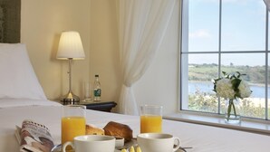 Ein Hotelzimmer mit Frühstücksbrett auf dem Bett, einer Lampe, einer Flasche und Blick ins Freie.