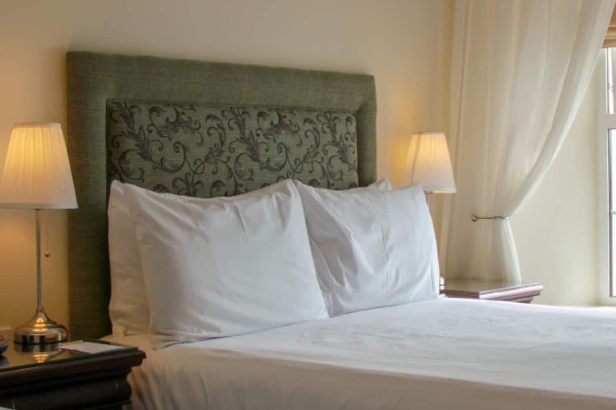 A neatly made bed with white linens, two bedside lamps, and a decorative headboard.