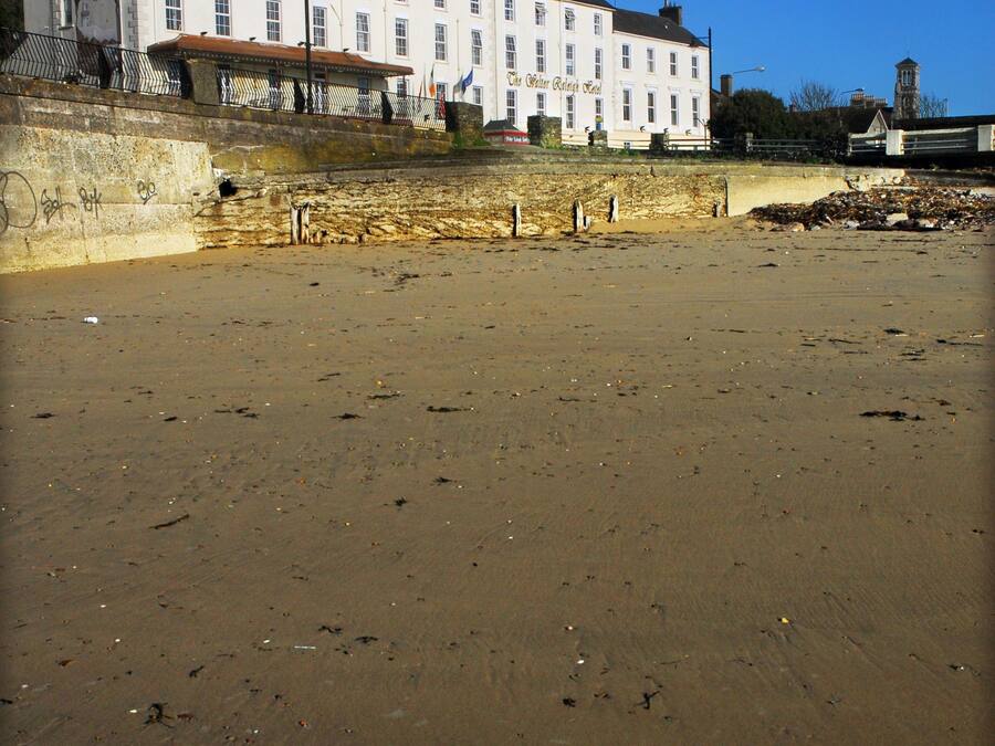 A large building with multiple windows and a flat roof, situated next to a sandy beach.