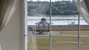 Ein Pavillon am Flussufer mit Blick auf eine Brücke und Grün im Hintergrund.