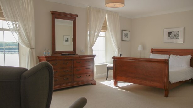 A bedroom with a wooden bed, a dresser, a chair, and a large mirror.