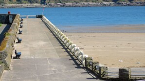 A stone pathway leading to a beach with benches and a flag.