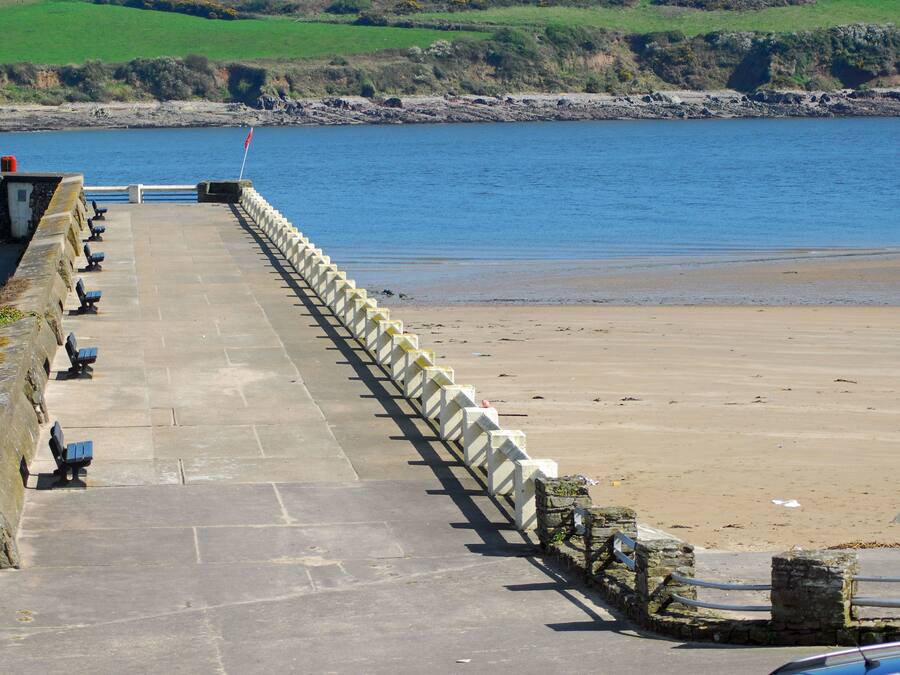 A stone pathway leading to a beach with benches and a flag.