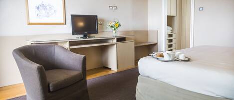A hotel room with a bed, a desk with a computer, a chair, and a tray with breakfast items.