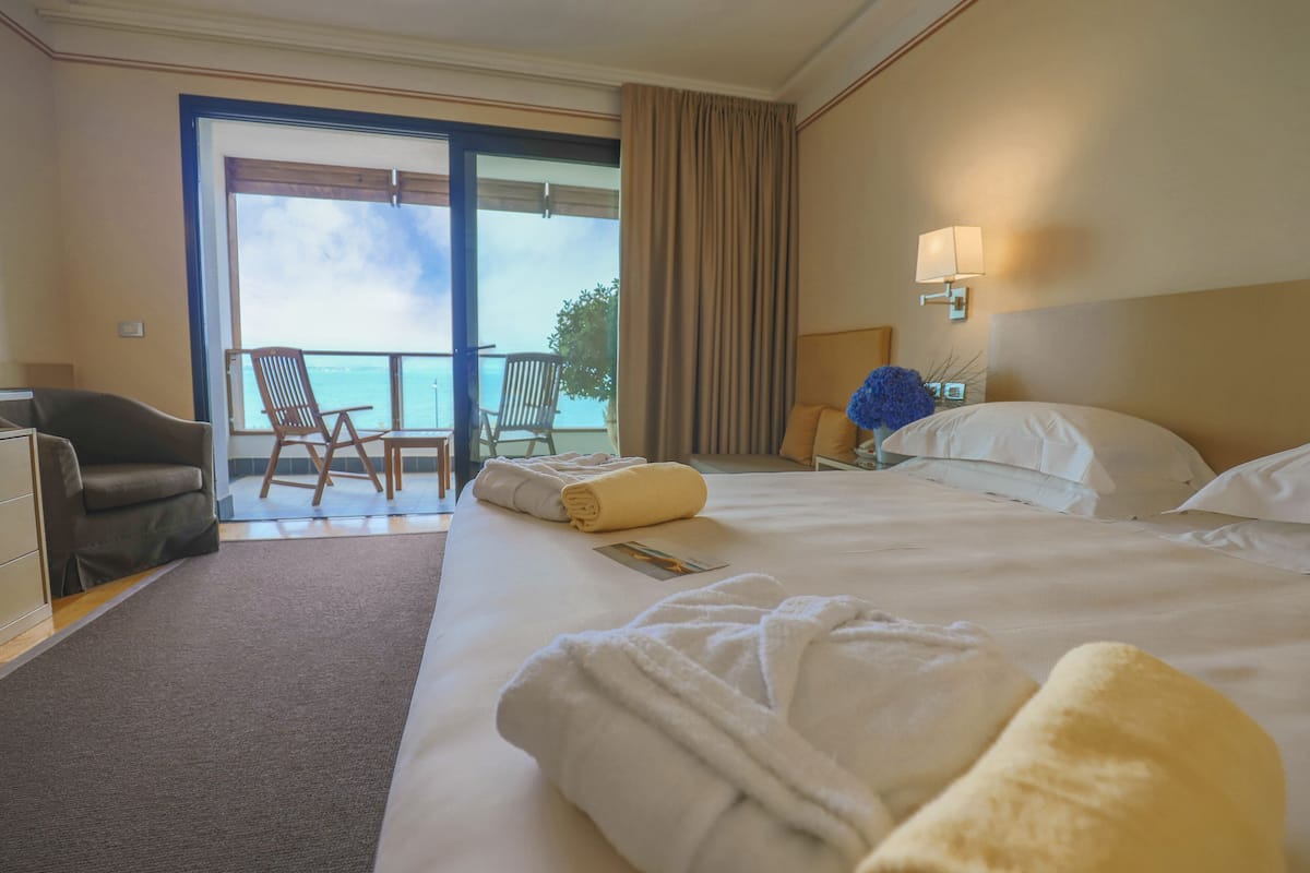 Habitación de hotel con una cama grande, dos sillas, un escritorio y vista al mar.