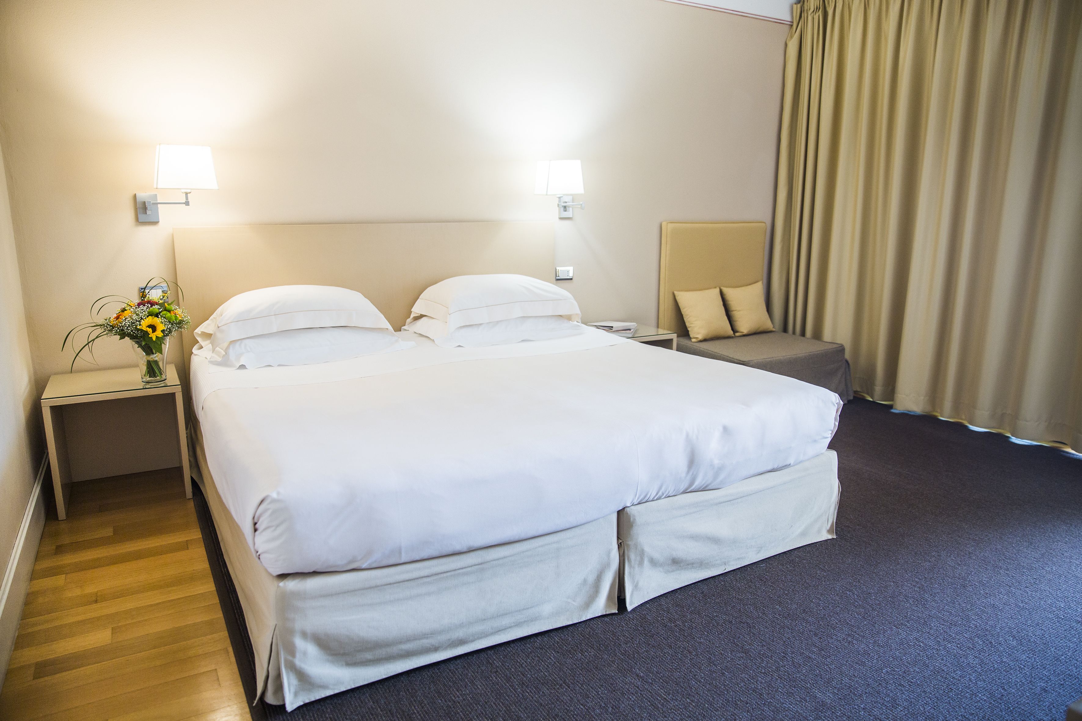 A hotel room with a large bed, two bedside tables, a nightstand, a chair, and a curtain.
