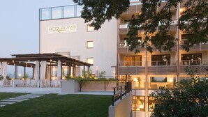 A hotel with a modern design, featuring a covered outdoor seating area with tables and chairs, a well-maintained lawn, and a balcony with potted plants. - Hotel Acquaviva del Garda (Desenzano del Garda)