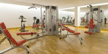 Un gimnasio con diversas máquinas de ejercicio, incluyendo una prensa de piernas y una prensa de pecho, además de un muro con espejos.