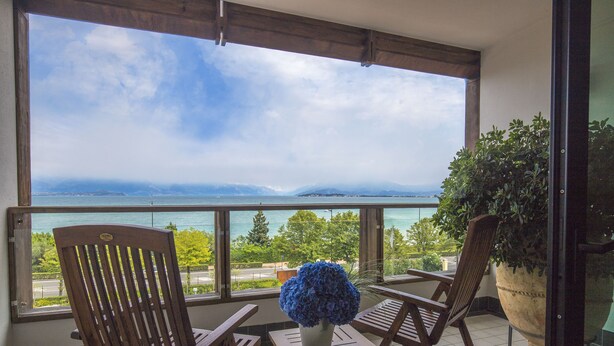 A balcony with two wooden chairs, a small table, and a potted plant. - Hotel Acquaviva del Garda (Desenzano del Garda)