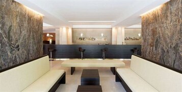 A modern lobby with a central seating area, marble walls, and a reception desk.