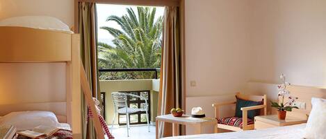 A hotel room with a balcony, a bed with a tray of breakfast items, a chair, a small table with a lamp, and a view of palm trees.