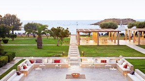 An outdoor seating area with a fire pit, a covered patio, and a view of the sea. - Grecotel Meli Palace (Agios Nikolaos)