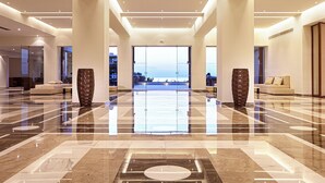 A spacious lobby with a polished marble floor, a central seating area, and a view of the sea through large windows. - Grecotel Meli Palace (Agios Nikolaos)