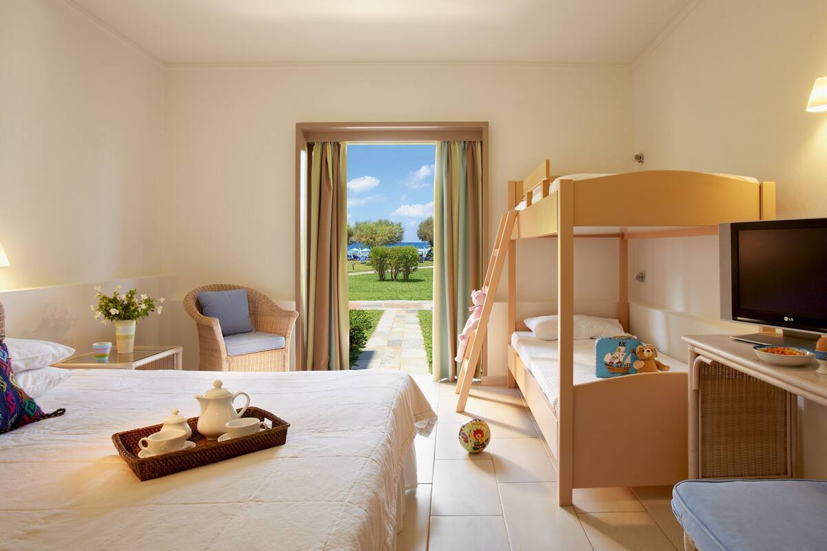 A hotel room with a bed, a desk with a TV, a bunk bed, and a view of the outdoors.
