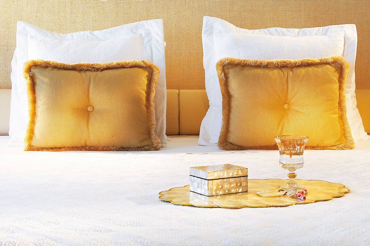 A neatly made bed with two square pillows, a small decorative box, and a glass on a round tray.
