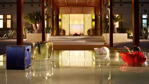 A modern hotel lobby with a reflective floor, a central seating area, and a view of the building's interior. - Grecotel Meli Palace (Agios Nikolaos)