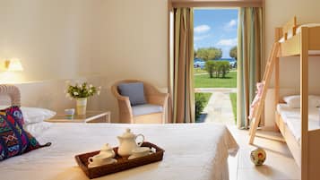 A hotel room with a bed, a wicker chair, a small table with a vase of flowers, and a view of the outdoors.