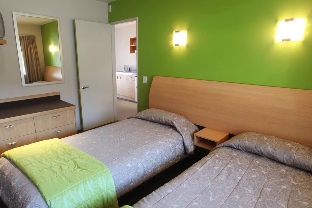 A room with two beds, a mirror, a dresser, and a green wall with two wall-mounted lights.