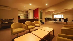 A conference room with tables and chairs, a kitchenette, and a red accent wall. - Park View Motor Lodge (Hamilton)