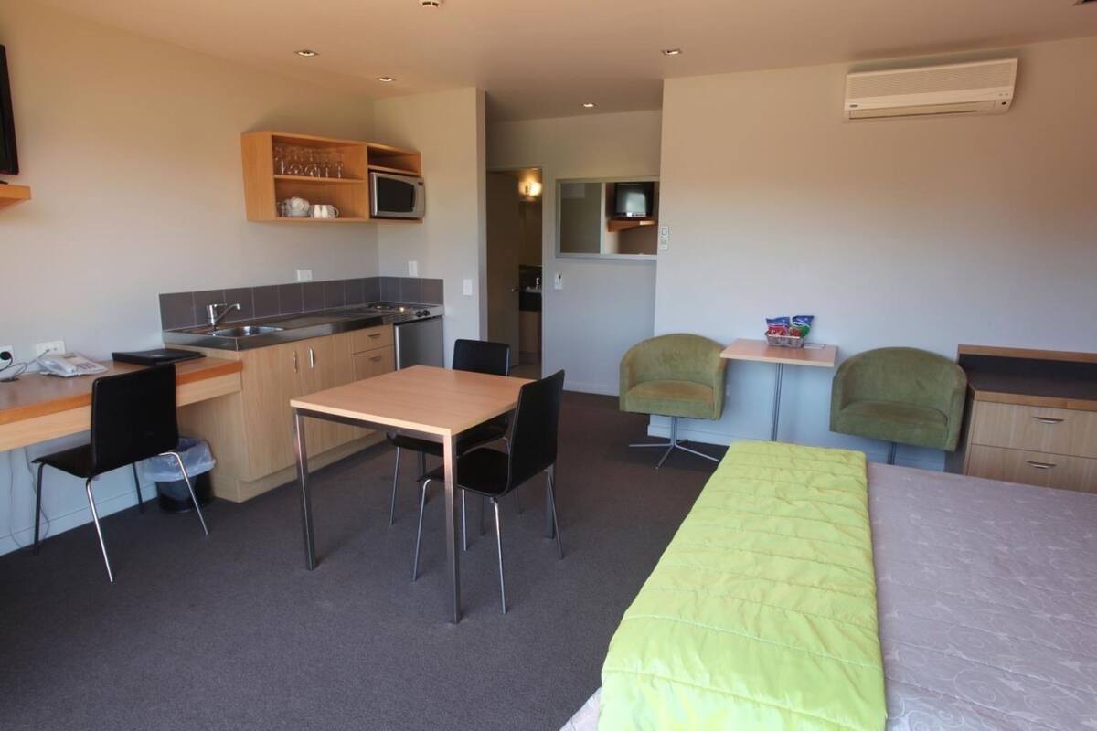 A compact hotel room with a kitchenette, a dining area, and a bed.