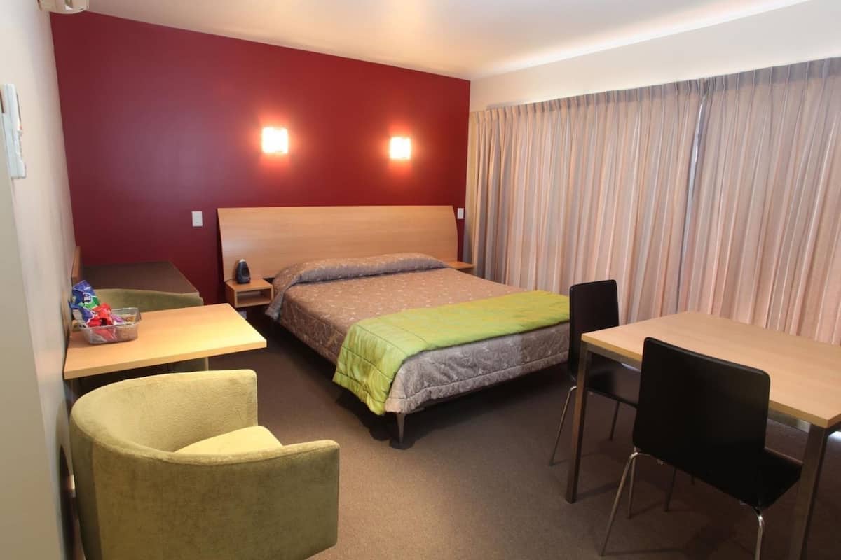 A hotel room with a bed, a desk, a chair, and a small table.