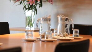 A dining table with a pitcher, glasses, and plates, set against a backdrop of flowers. - Park View Motor Lodge (Hamilton)