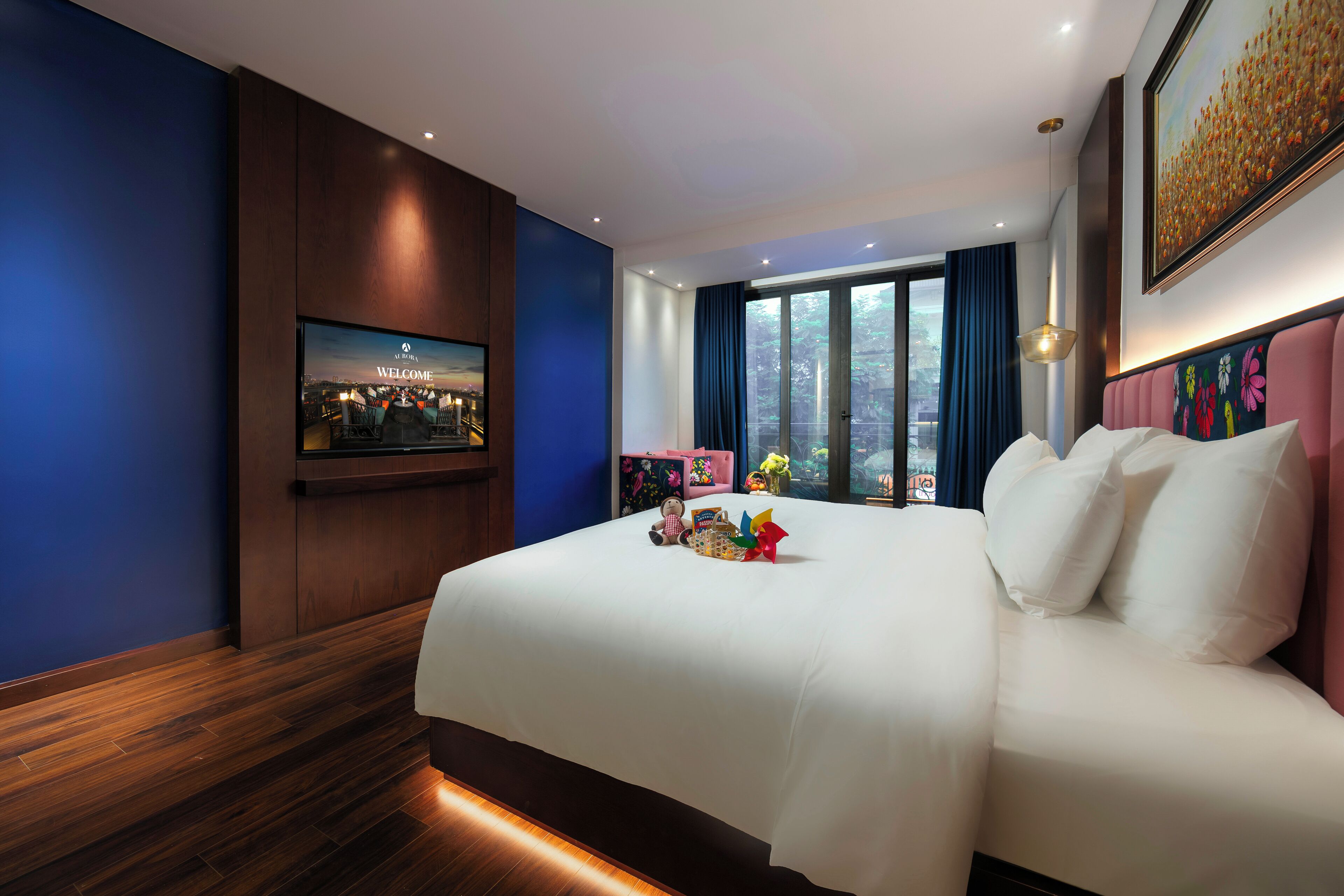 Habitación de hotel con una cama grande, televisor montado en la pared y ventana con cortinas.