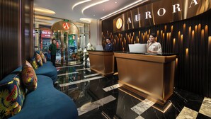 A modern hotel lobby with a reception desk, a seating area with colorful cushions, and a check-in counter. - Aurora Central Hotel  (Hanoi)