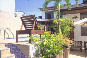 A poolside area with a wooden chair, a small table, and a wooden planter with plants.
