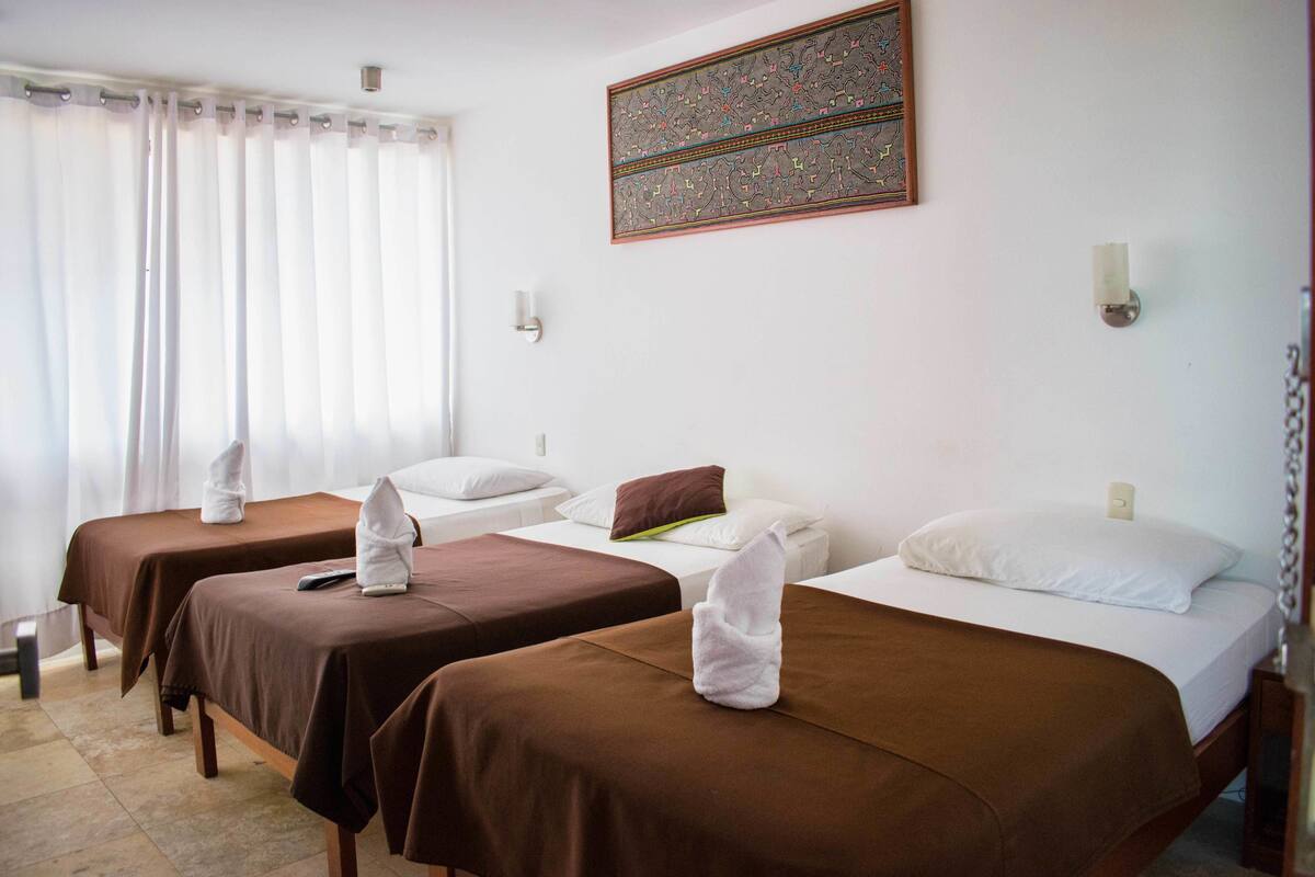 Una habitación de hotel con dos camas individuales, cada una con una colcha marrón y almohadas blancas, una mesita con un control remoto y un adorno en la pared.