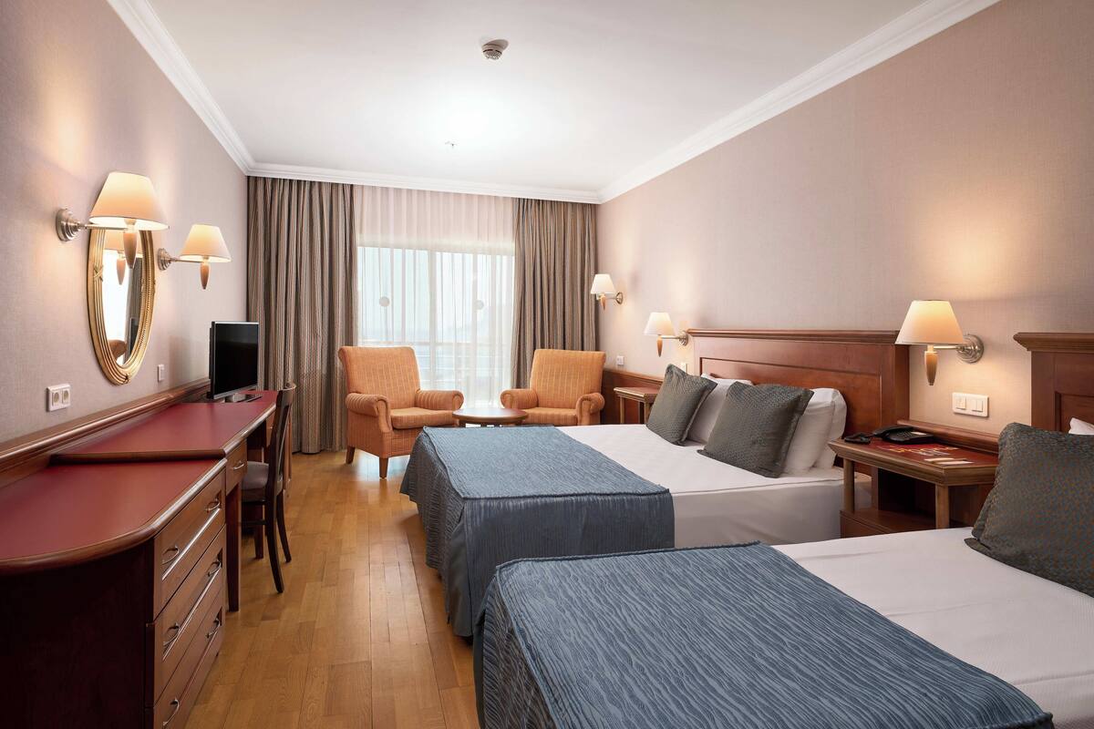 A hotel room with two beds, a desk, a chair, a TV, and a window with curtains.
