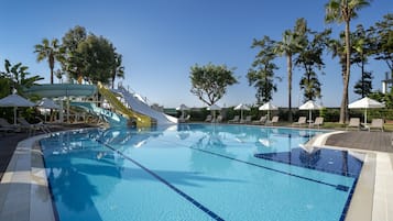 Relax by the pool surrounded by palm trees and lounge chairs, with a water slide nearby for added fun.