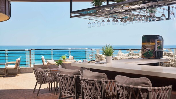 An outdoor bar area with wicker chairs, a bar counter, and a view of the ocean. - Grand Kaptan Hotel - Ultra All Inclusive (Alanya)