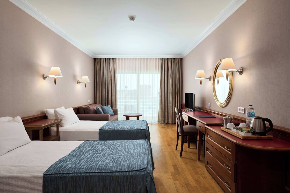 A hotel room with two beds, a desk, a chair, a dresser, and a large mirror.