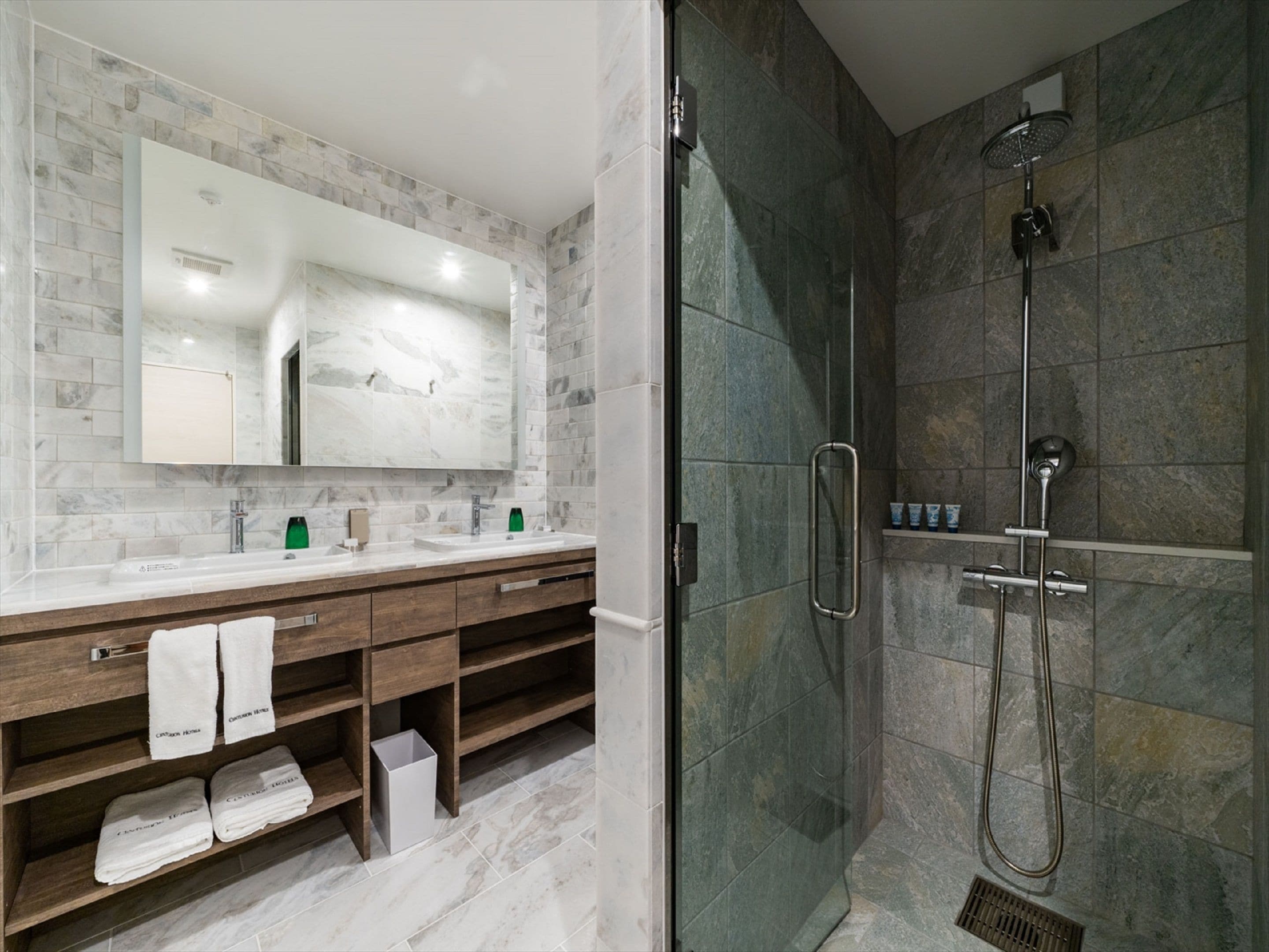 A modern bathroom with a large mirror, dual sinks, and a shower area.