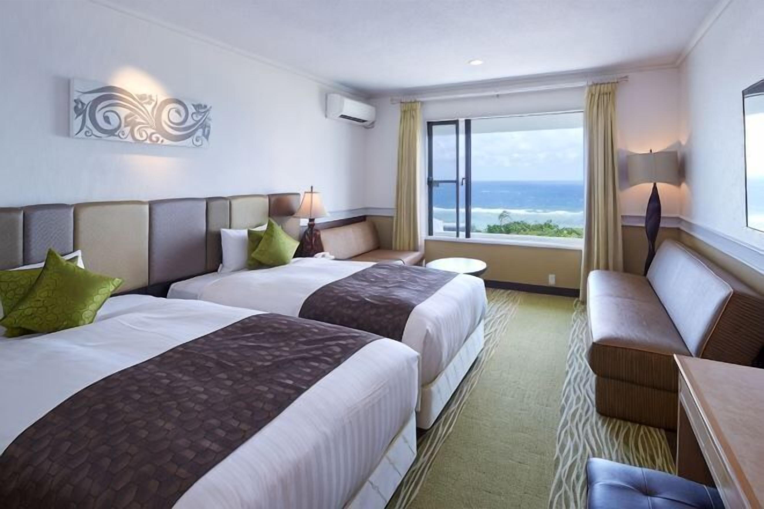 A hotel room with two beds, a sofa, a small table, and a view of the ocean.