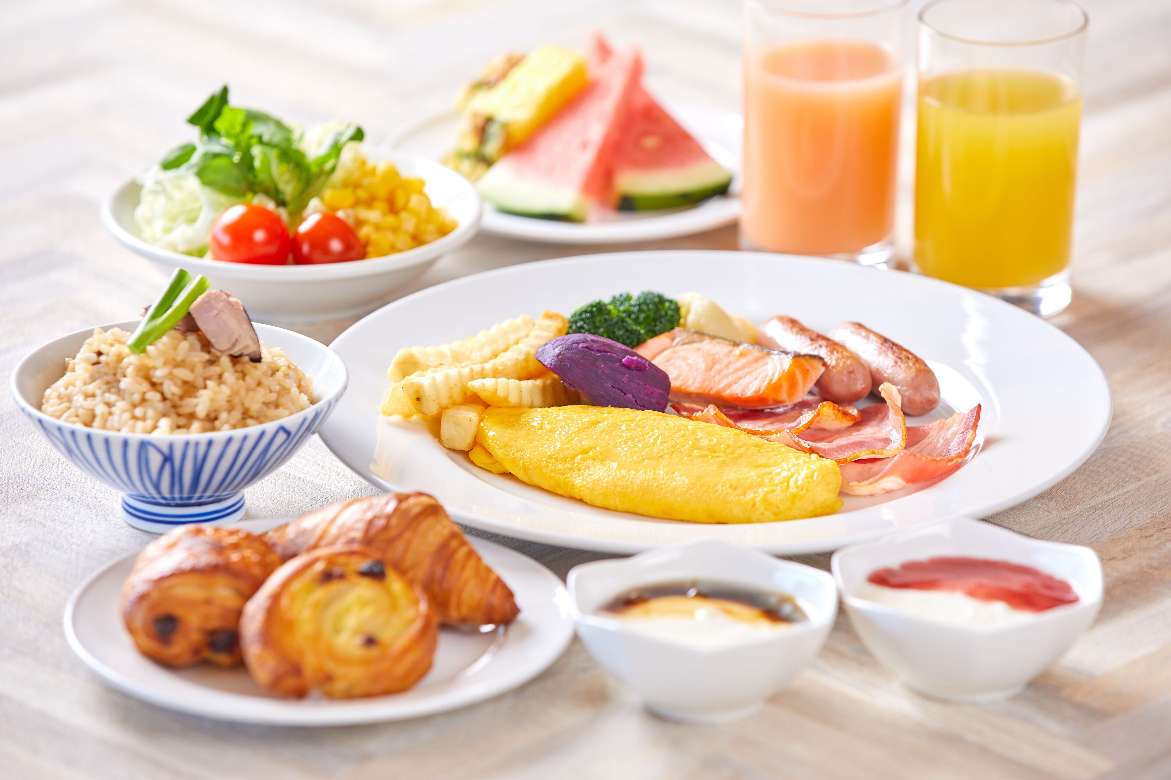 Un desayuno abundante con diversos platos, como huevos, jamón y bollería, junto con frutas frescas y jugos.