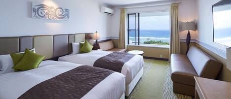 Habitación de hotel con dos camas, zona de estar y un ventanal con vistas al océano.