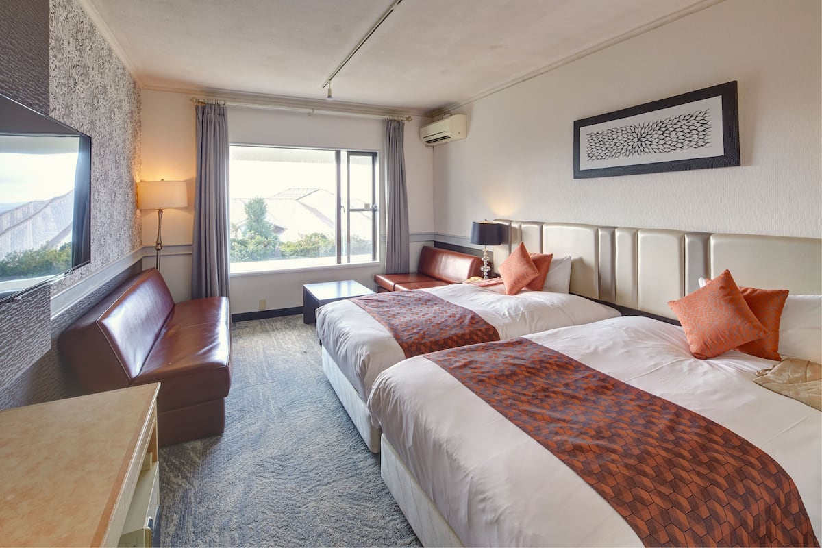 A hotel room with two beds, a sofa, a desk, and a large window.