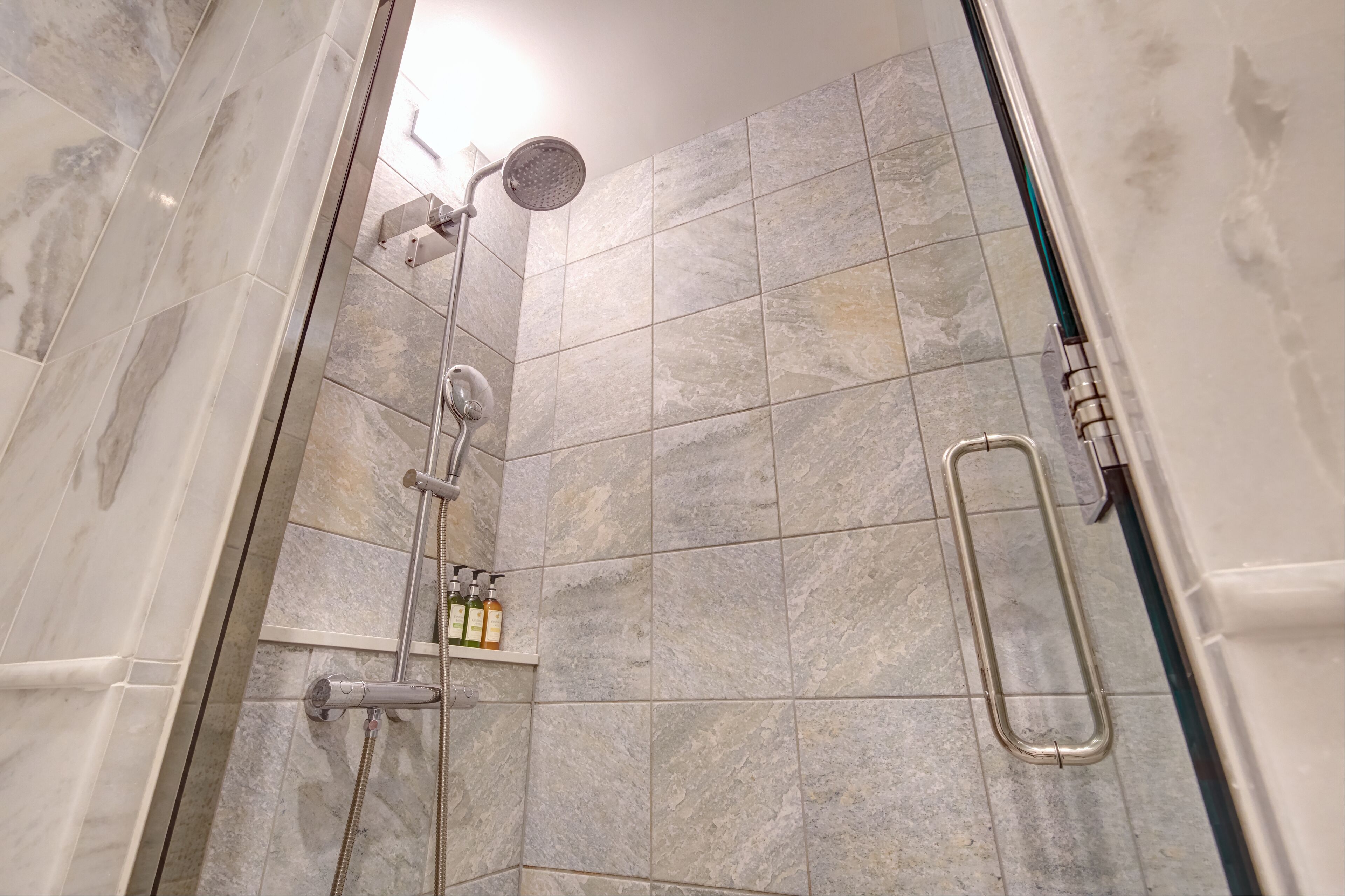 A shower area with a handheld showerhead, a wall-mounted showerhead, and a grab bar.