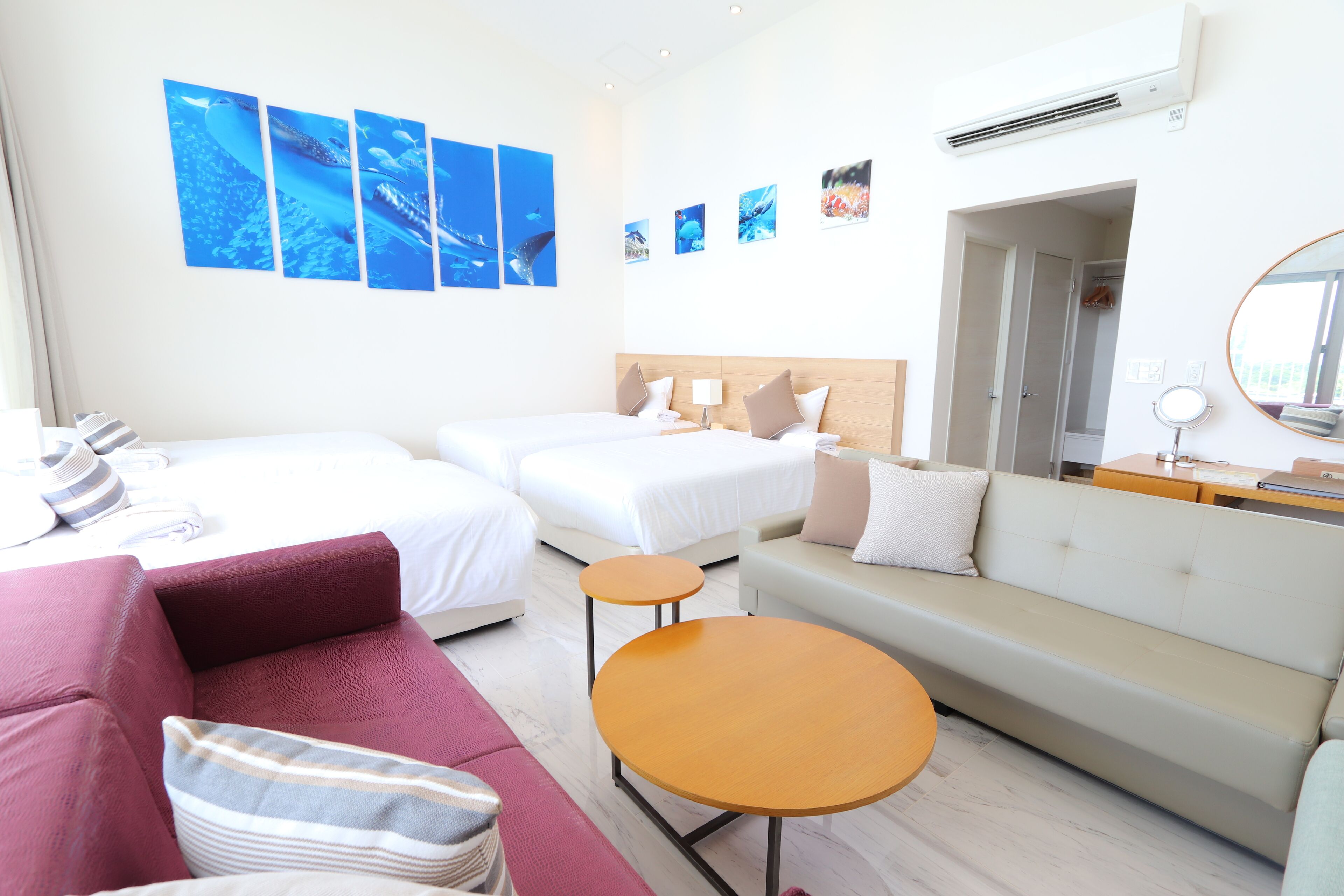 A hotel room with two beds, a sofa, a round table, and artwork on the wall.