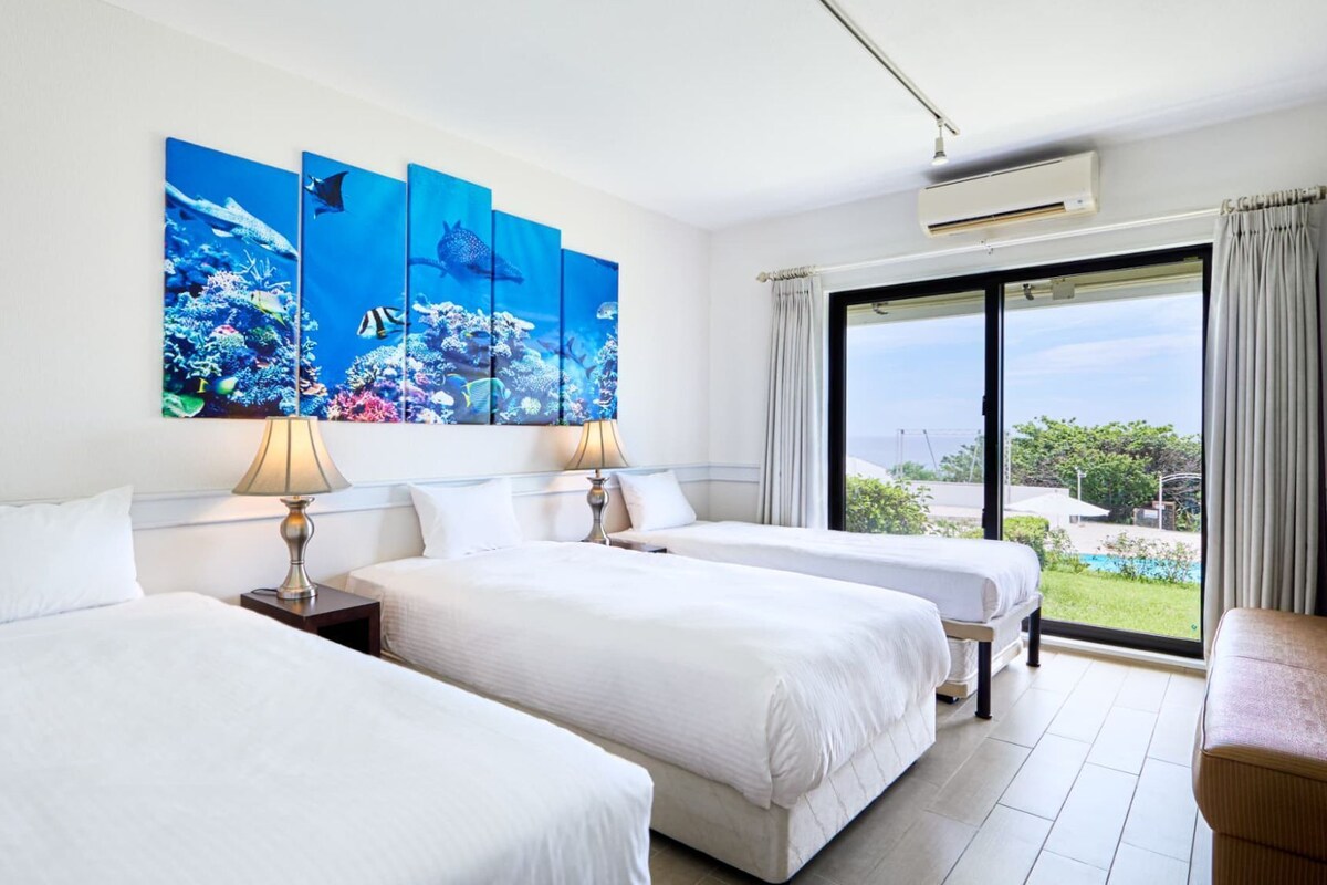 A hotel room with two beds, a large window, and a view of the outdoors.
