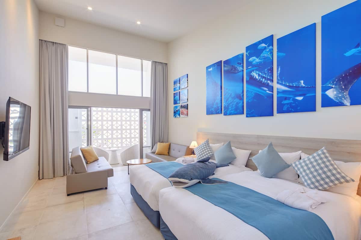 A hotel room with a large bed, a sofa, a TV, and artwork on the wall.