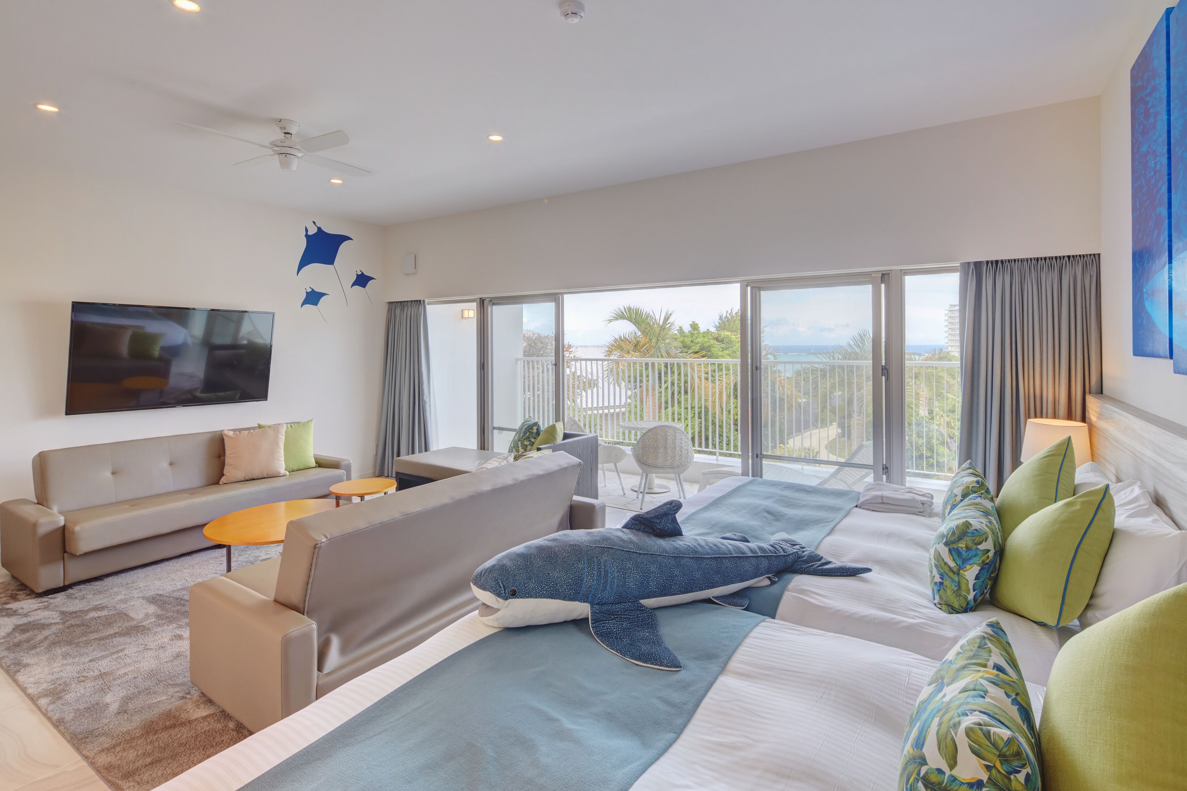 Une chambre d’hôtel moderne dotée d’un grand lit, d’un canapé, d’une télévision et d’un balcon offrant une vue sur la mer.