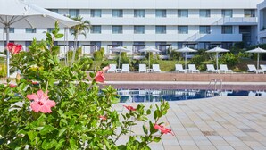 Un hotel con piscina, sombrillas blancas y sillas de descanso.