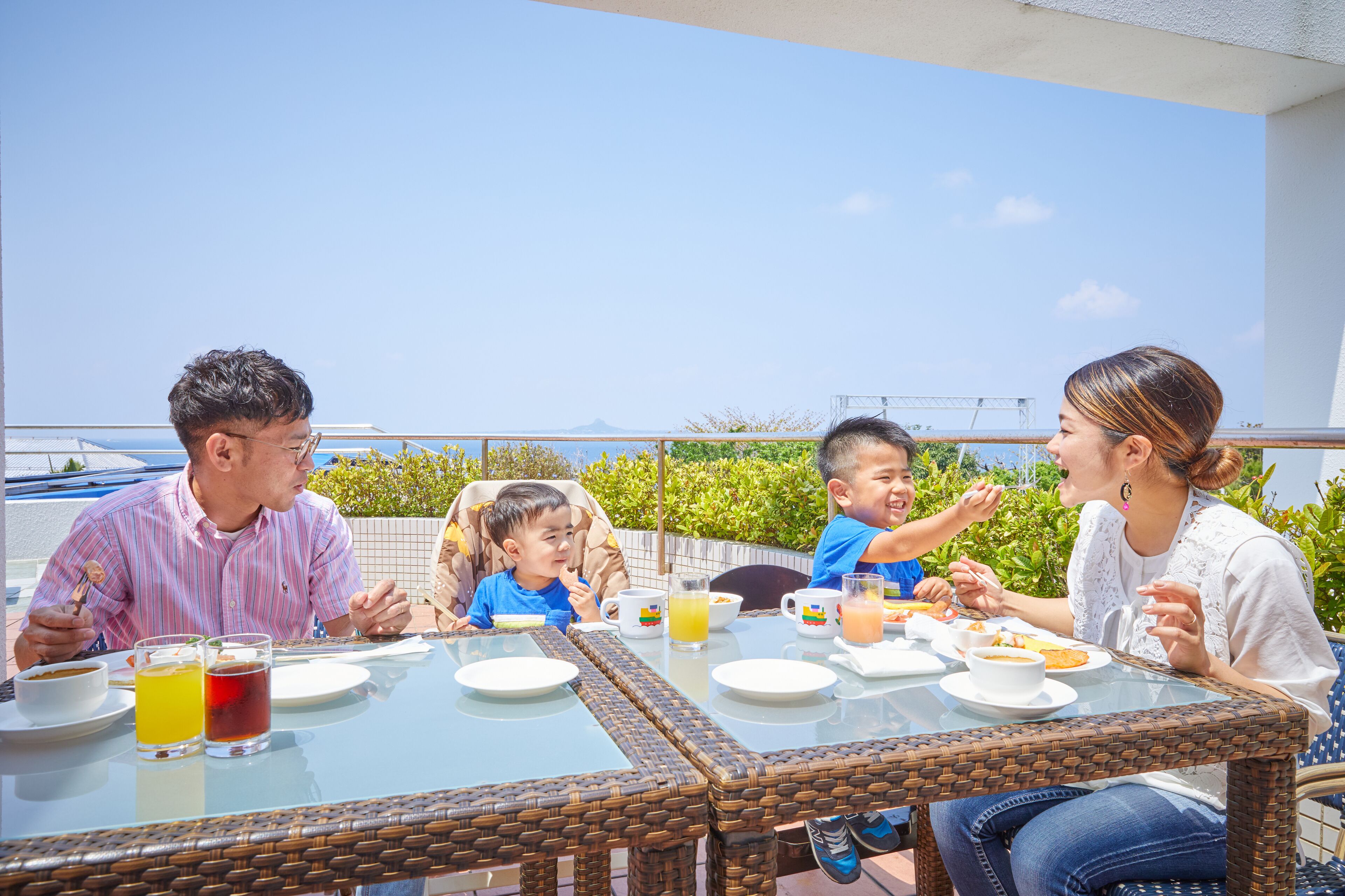 Una familia cenando en una mesa al aire libre, con cielo despejado y vegetación de fondo.